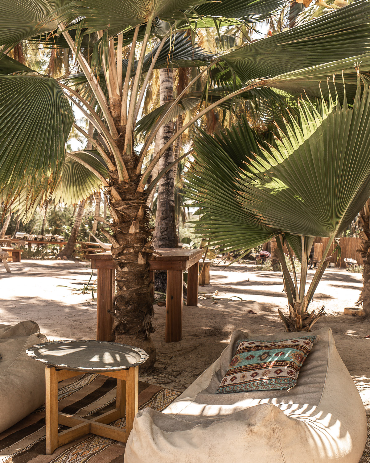 Bohemian floor cushions, rugs, and furniture underneath palm trees on the sand, featured at Eteka Beach Longe & Hotel - Cartagena, Colombia